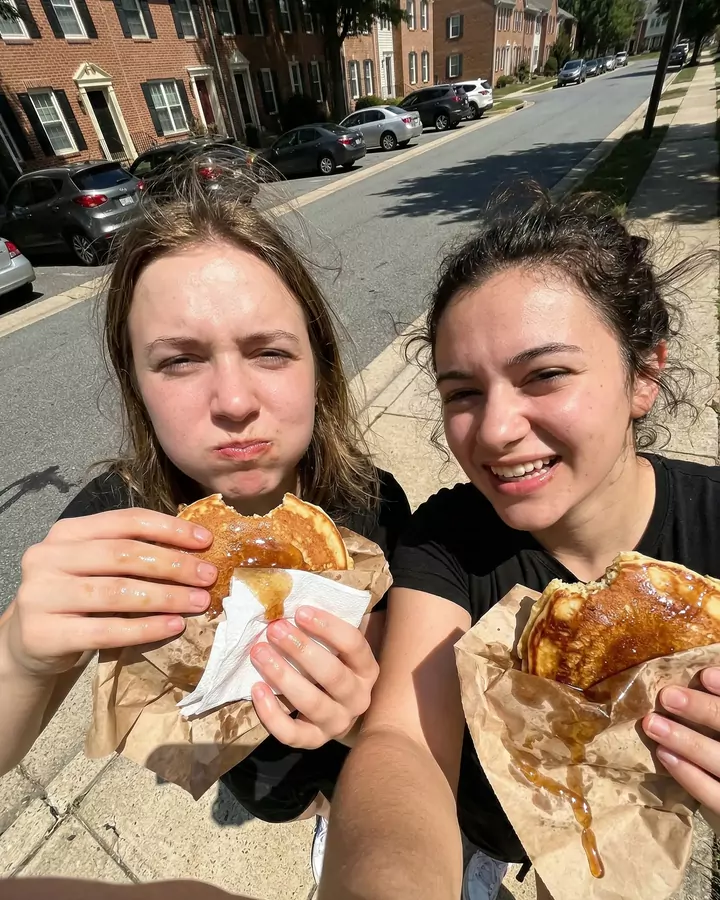 Two friends on a kerb, mid-bite, laughing